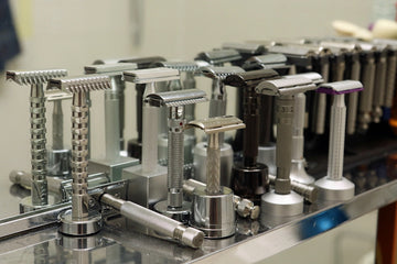 Various metal safety razors displayed on a reflective surface.