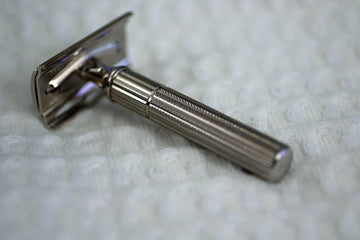 A classic silver safety razor on a textured white surface.