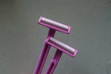 Two pink disposable razors held against a plain grey background