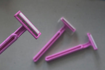 Three pink disposable razors arranged on a plain grey surface