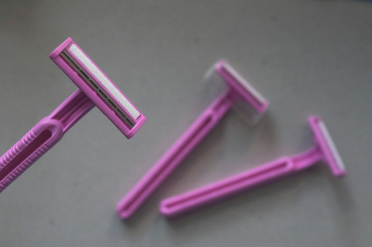 Three pink disposable razors arranged on a plain grey surface